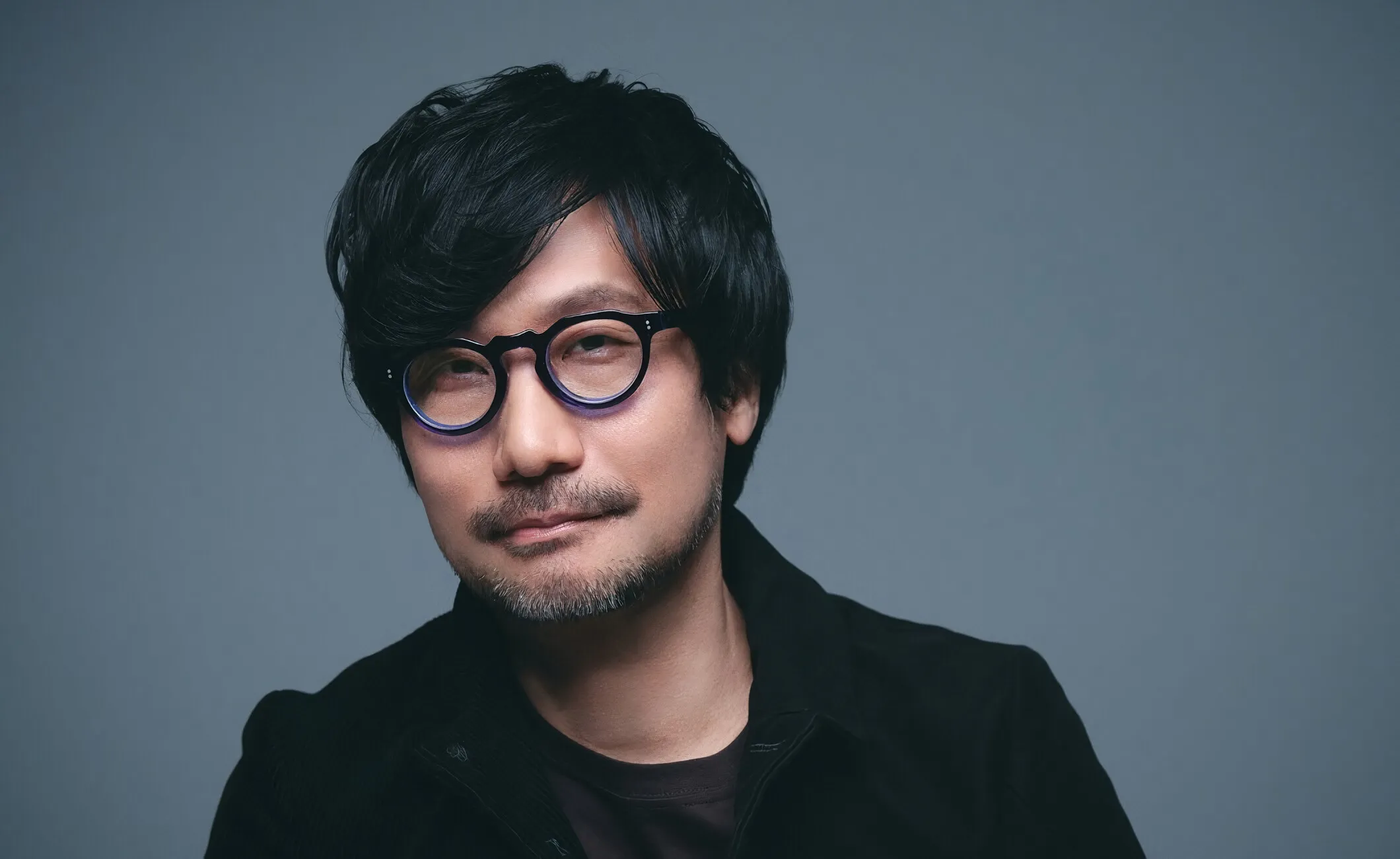 Hideo Kojima, criador de Metal Gear e Death Stranding, posa para retrato com expressão serena. O visionário japonês redefiniu os videogames ao unir cinema, filosofia e emoção, e participa da Brasil Game Show 2025.